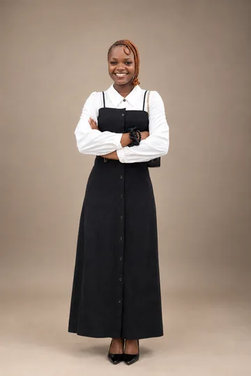 Julius Omolara smiling with arms crossed in a white blouse and black dress against a warm studio backdrop